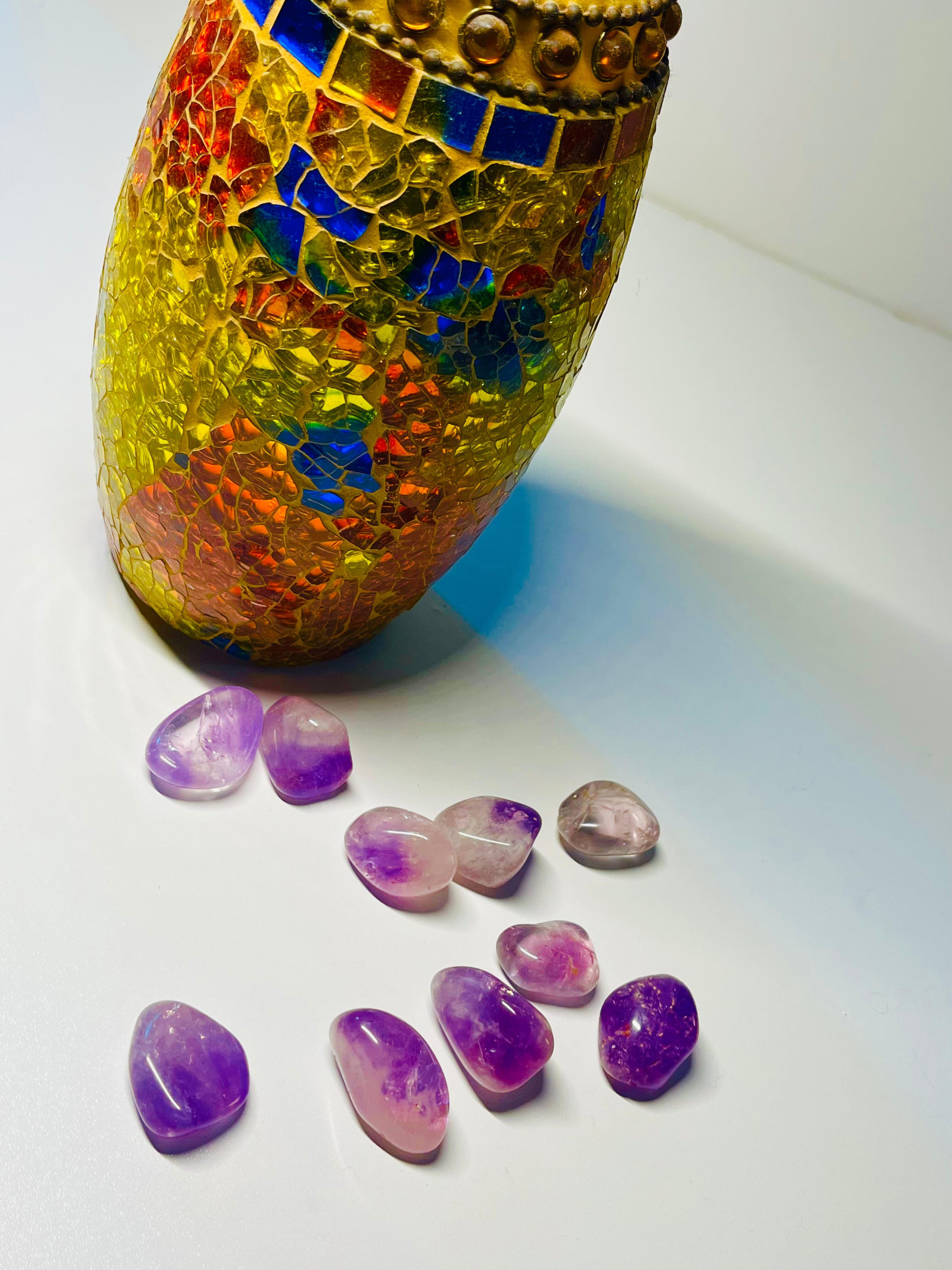 Amethyst tumbles on a table with a vase behind it
