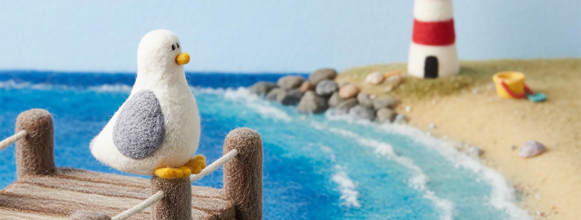 "A charming needle-felted seagull perched on a rustic wooden pier overlooking a seaside scene, featuring a needle-felted lighthouse, sandy beach, and blue wool-textured waves in a 16:9 landscape format."