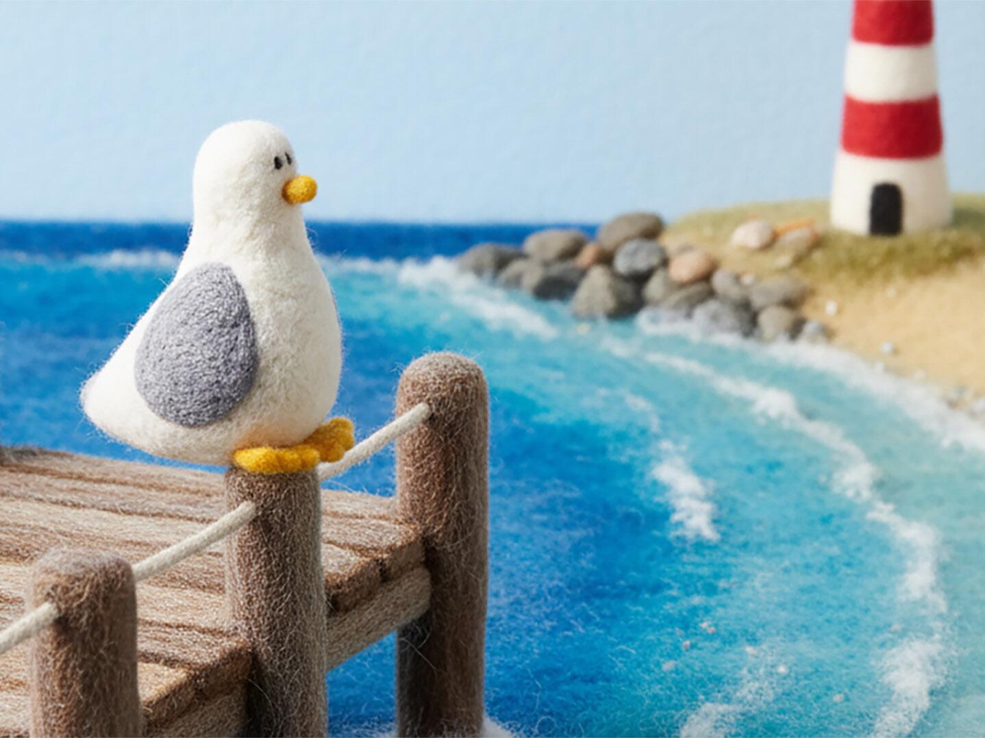 "A charming needle-felted seagull perched on a rustic wooden pier overlooking a seaside scene, featuring a needle-felted lighthouse, sandy beach, and blue wool-textured waves in a 16:9 landscape format."