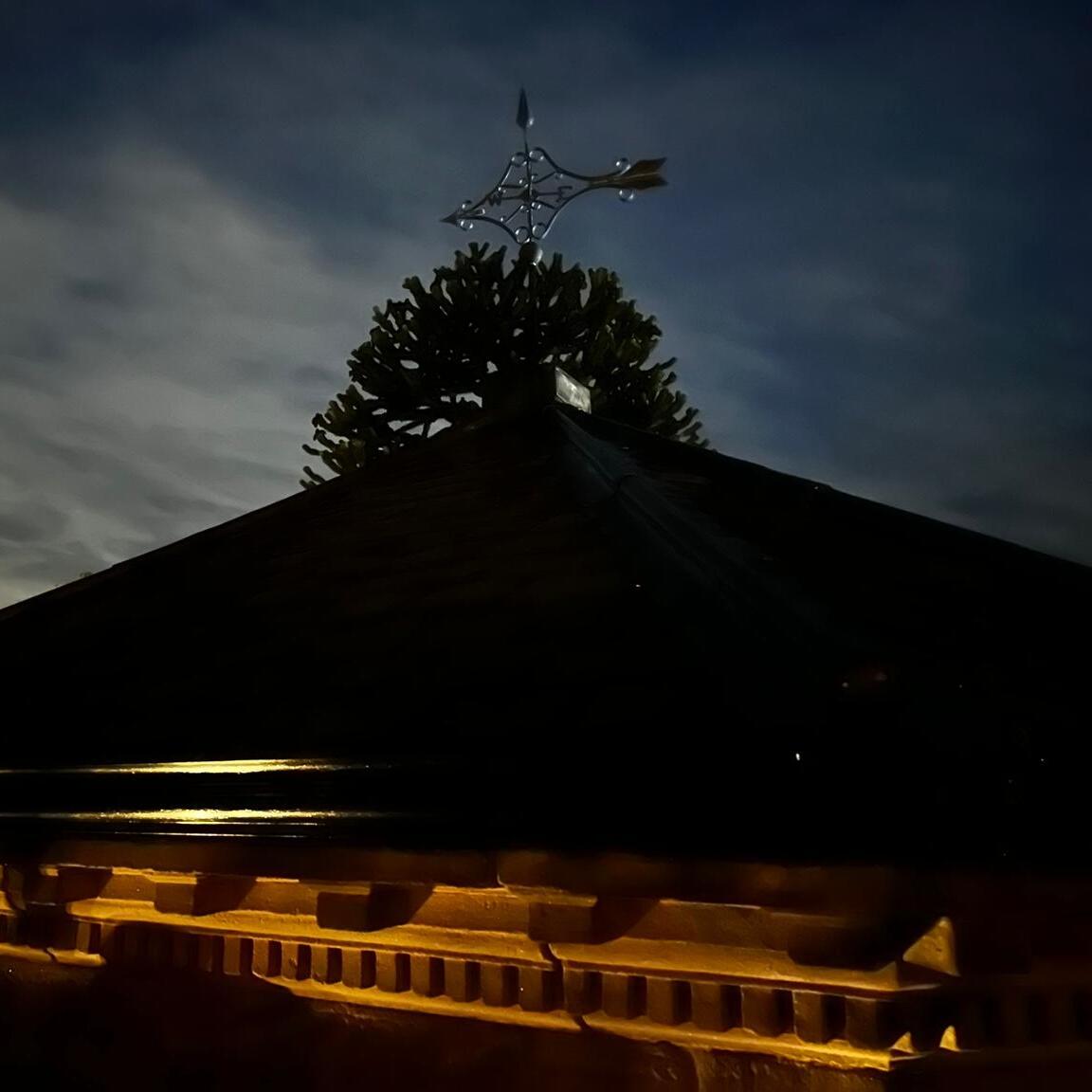 Large copper Victorian arrow weathervane silhouetted against a dramatic night sky on a historic stone building in the UK