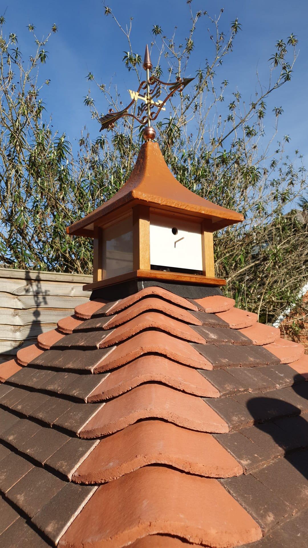 Close up of polished copper Victorian arrow weathervane on the apex of a hexagonal tiled dovecote turret roof
