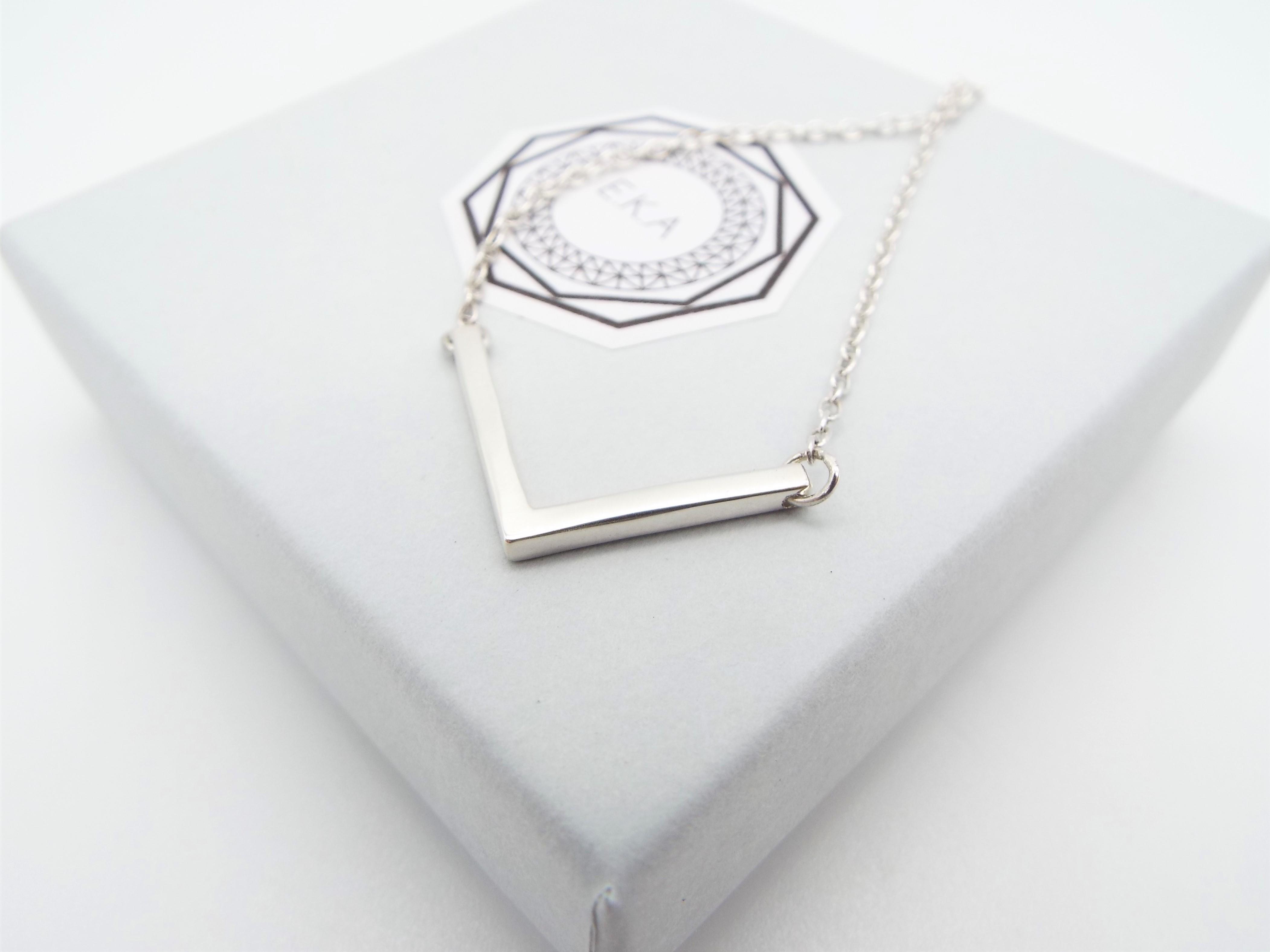 silver v shaped necklace on a box