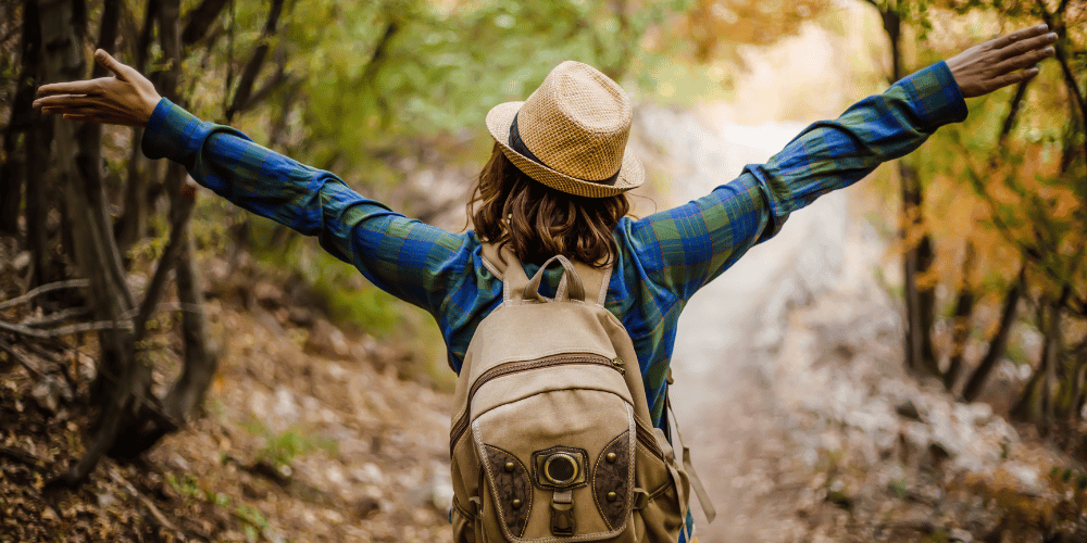 Person walking outdoors in nature with arms outstretched, representing natural wellbeing, movement and healthy body balance.