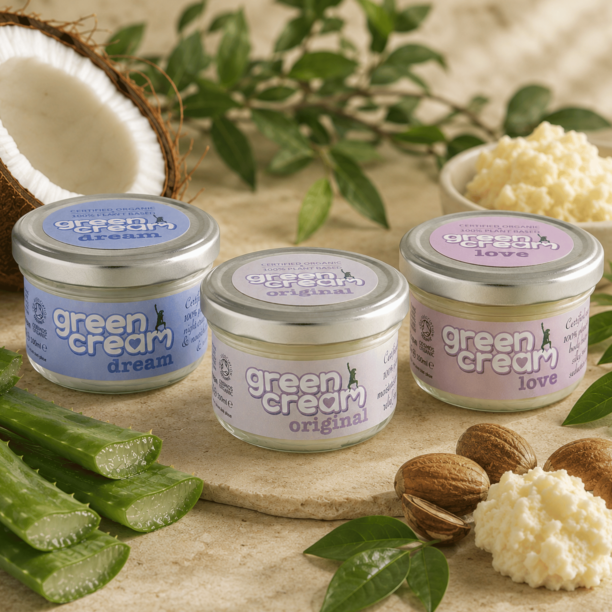 Three Green Woman Green Cream organic moisturisers (Original, Dream and Love) displayed together on a natural stone surface, surrounded by fresh aloe vera, coconut, shea butter and botanical leaves, highlighting the plant-based ingredients and certified organic skincare range.