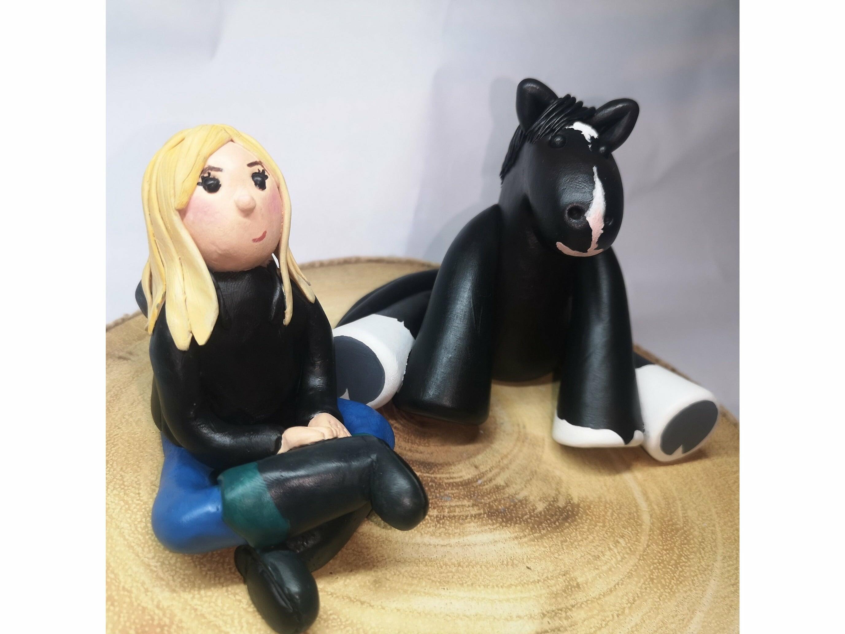A clay model of a blonde girl in stable gear sitting next to a black cob