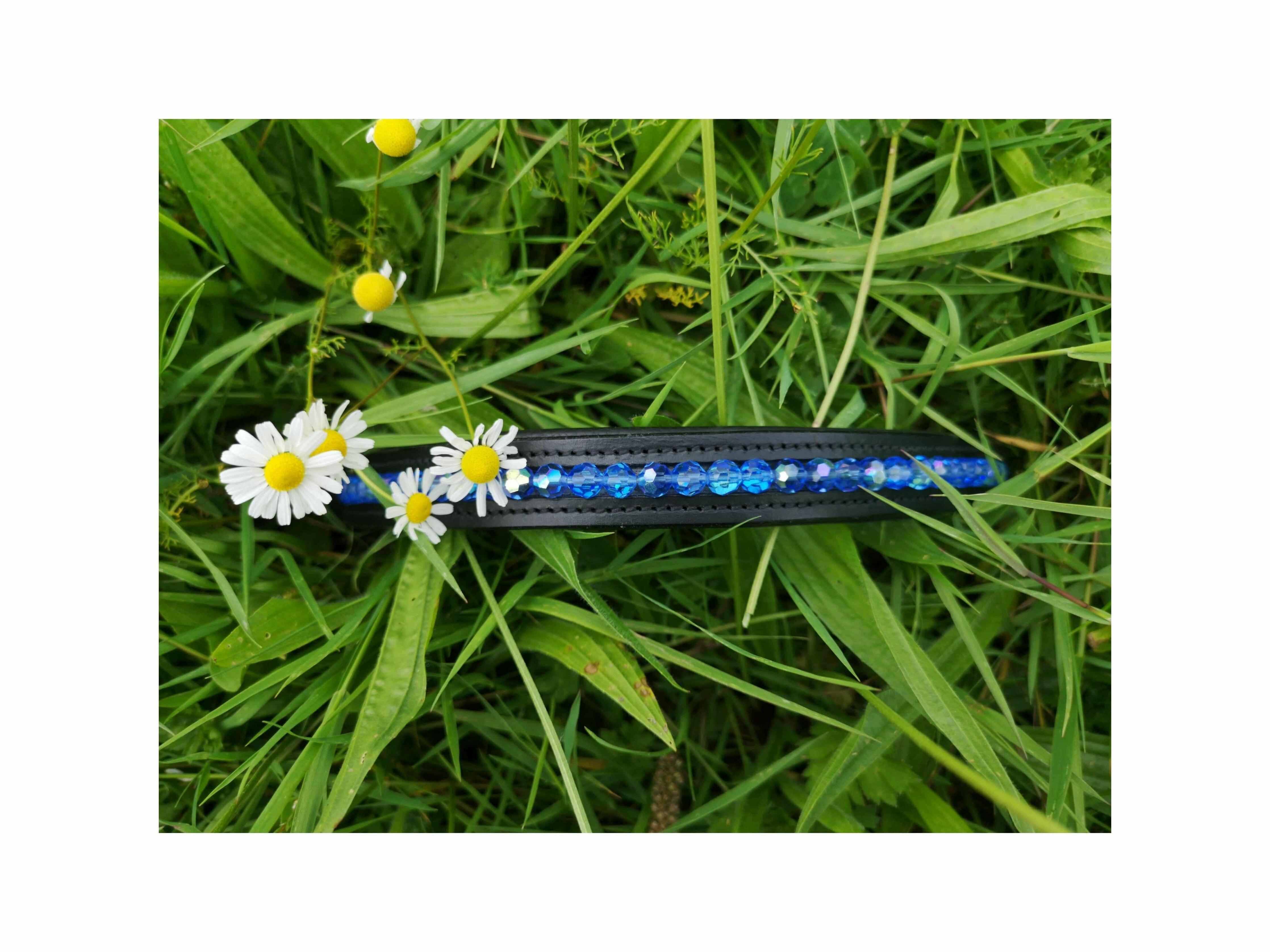 Browband with hand stitched blue faceted glass beads laying on long grass