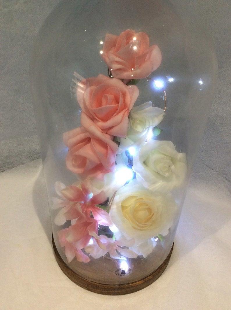 Glass Dome, Wooden Base, Flowers, Lights  Beauiful Flower Dome with Lights and Flowers.  Freestanding on its own base, with litle feet where the Battery power pack will be hidden  Lots of Flowers made of Silk and foam in this glass dome display  Product size Height: 27 cm Diameter: 14 cm  Base: Solid acacia, Oil Basematerial: Glass