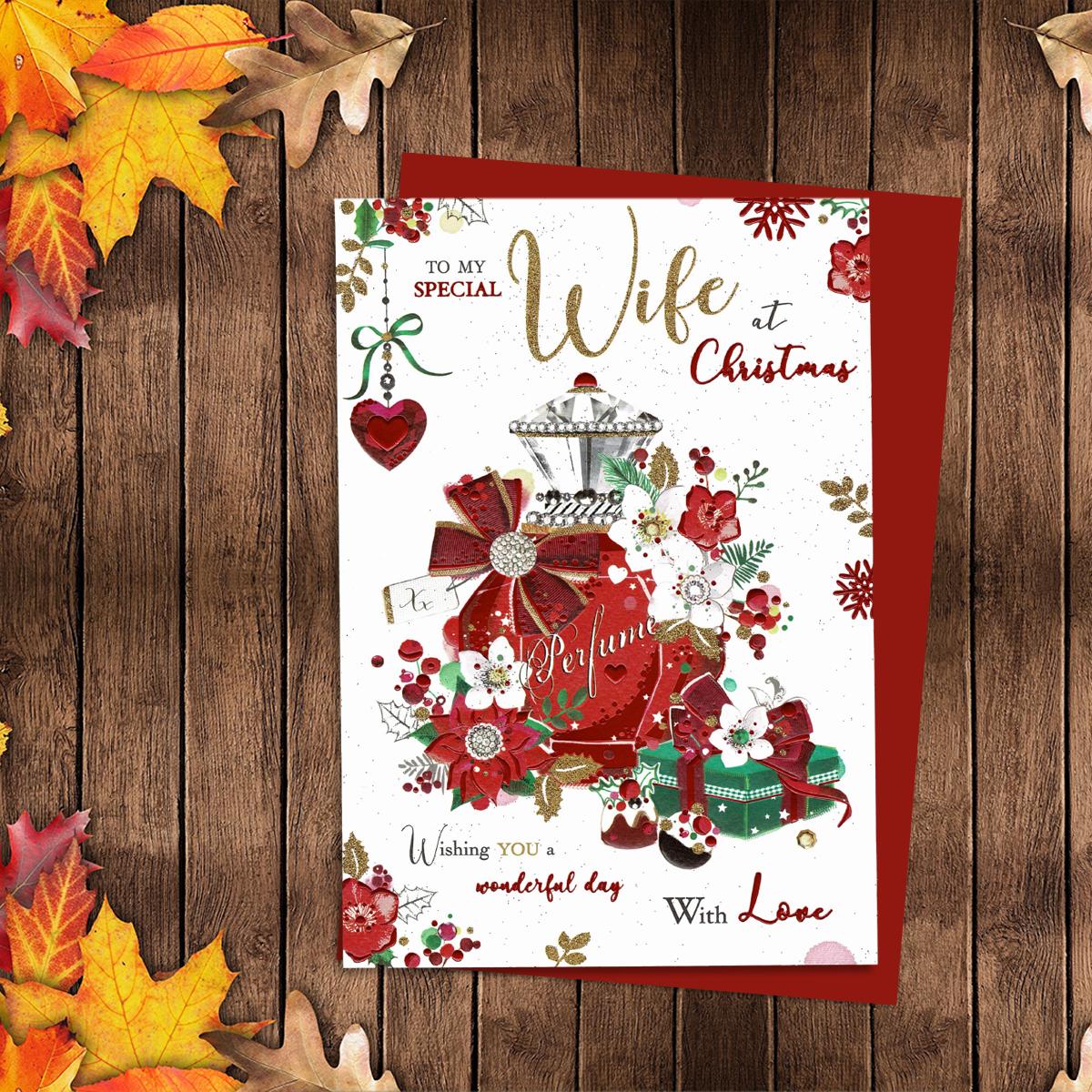 To My Special wife At Christmas Showing A Beautiful decorated perfume Bottle With Wrapped Gifts And Poinsettias. Finished With Gold Glitter Lettering, Red Foil Details And Red Envelope