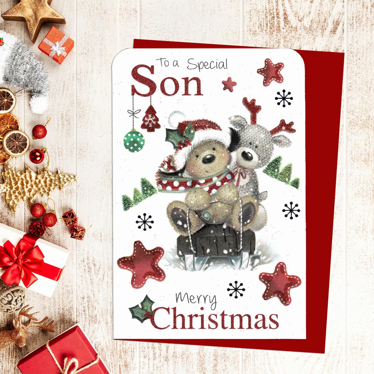 To A Special Son Merry Christmas Showing Two Dogs On A Sled Surrounded By Baubles And Stars. Red Glitter Lettering And Red Envelope Complete The Look
