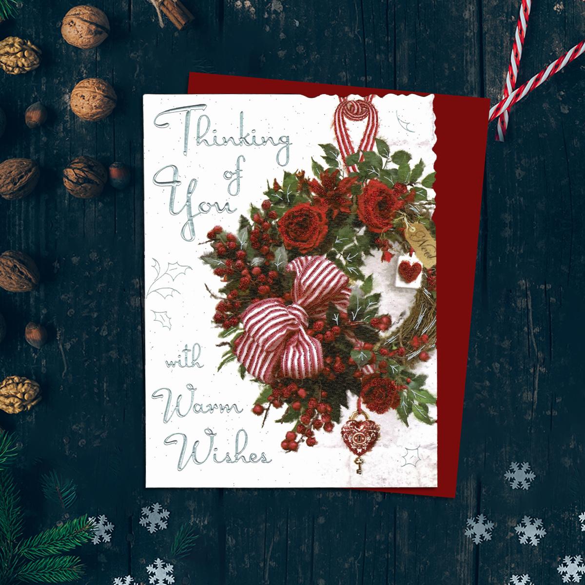 Thinking Of You With warm wishes Featuring A Christmas Wreath Filled With Red Roses, Berries And Hearts. Finished With Silver Foil Detail, Red Glitter and Red Envelope