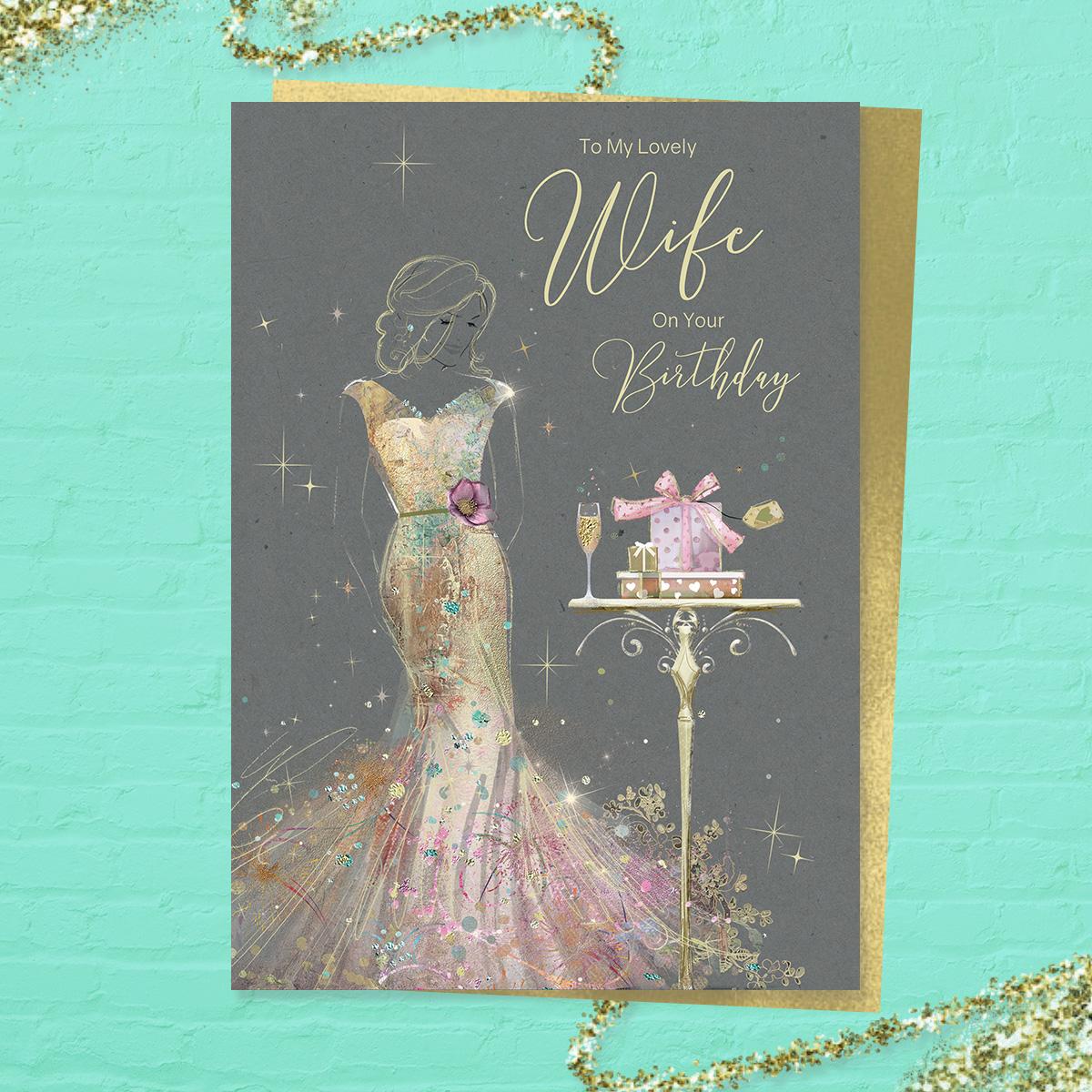 'To My Lovely Wife On Your Birthday' card featuring a beautiful lady in a long gold dress with champagne and gifts. With added sparkle and gold foil detail. Colour image inside with heartfelt verse. Complete with gold colour envelope