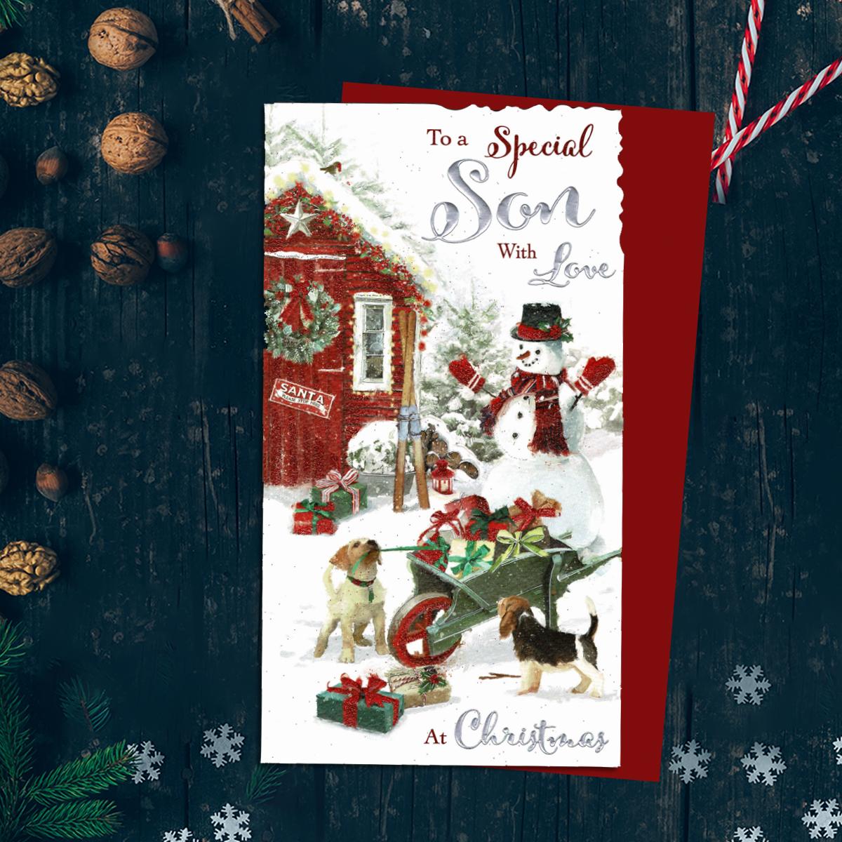 To A Special Son With Love At Christmas Showing a Snowman , Wheelbarrow Full Of Gifts And Two Dogs Pulling At The Gift Ribbon! Finished With Silver Foil And Red Glitter detail And With Red Envelope