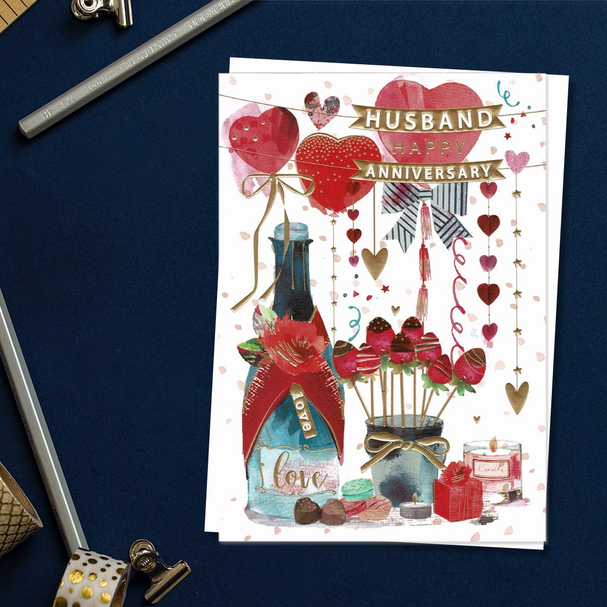 ' Husband Happy Anniversary' Card Featuring Balloons, Champagne, Dipped Strawberries And Gifts! Enhanced With Gold Foil Detail And Complete With White Envelope