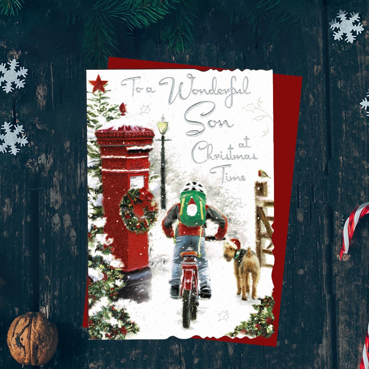 To A Wonderful Son At Christmas Time Featuring A Boy Riding A Bicycle Past A Decorated Post Box In The Snow. A  Dog Looks On. Finished With silver Foil lettering, Red Glitter and Red Envelope