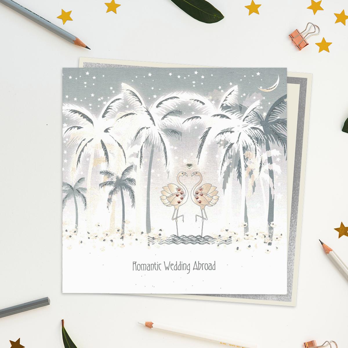A Stunning, Luxury, Handcrafted Wedding Day Card In Soft Grey With Pink Showing Sparkling Palm Trees And Two Jewelled Flamingos On The Beach. Caption: Romantic Wedding Abroad. With Biodegradable Glitter And Compostable Wrap. Blank Inside For Own Message. Warm White Envelope With Silver Border.