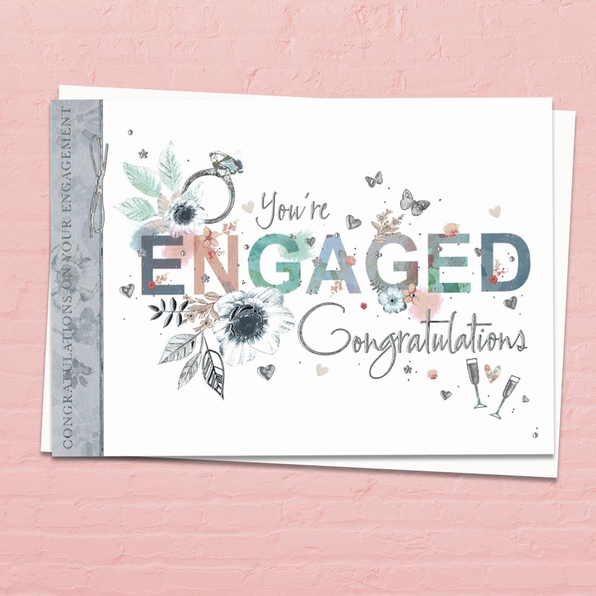 'You're Engaged Congratulations' Card. This 'Landscape' Card Features A Diamond Ring with Beautiful Floral Adorned Letters Of 'Engagement' . With Beautiful Silver Foil Detail And White Envelope