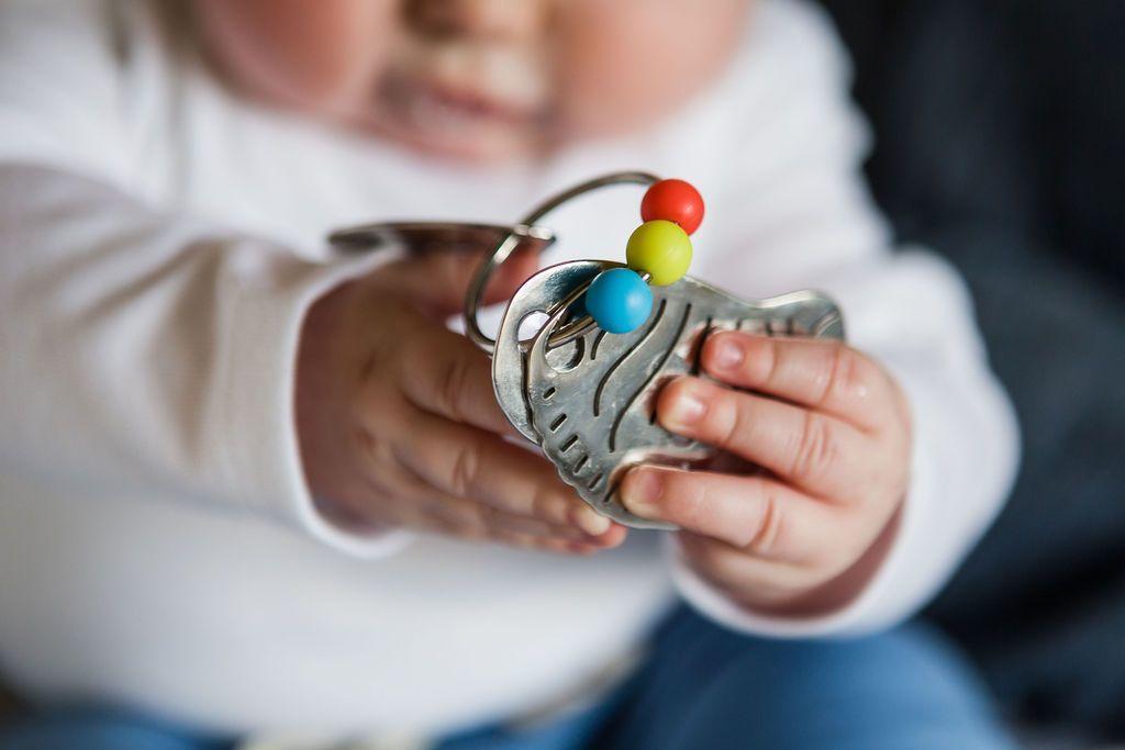 Baby's hands holding stainless steel key-shaped teether.