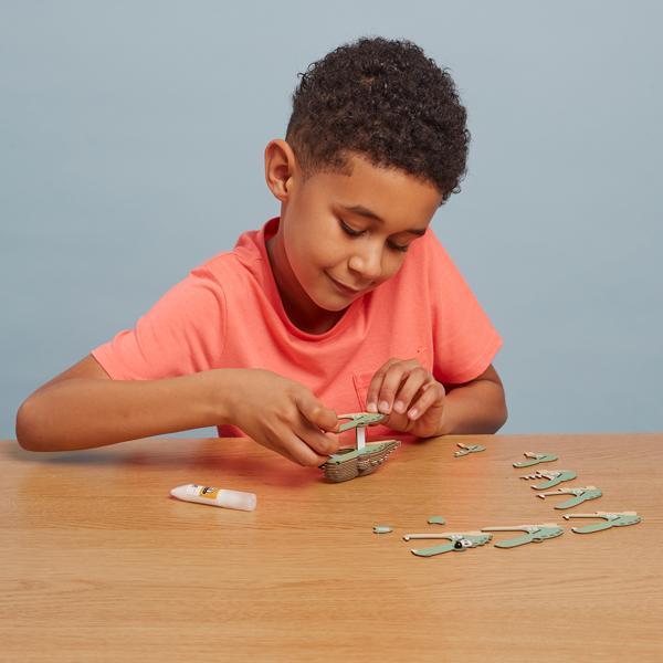 Boy with dark hair and peachy tshirt putting the alligator model together using craft glue.