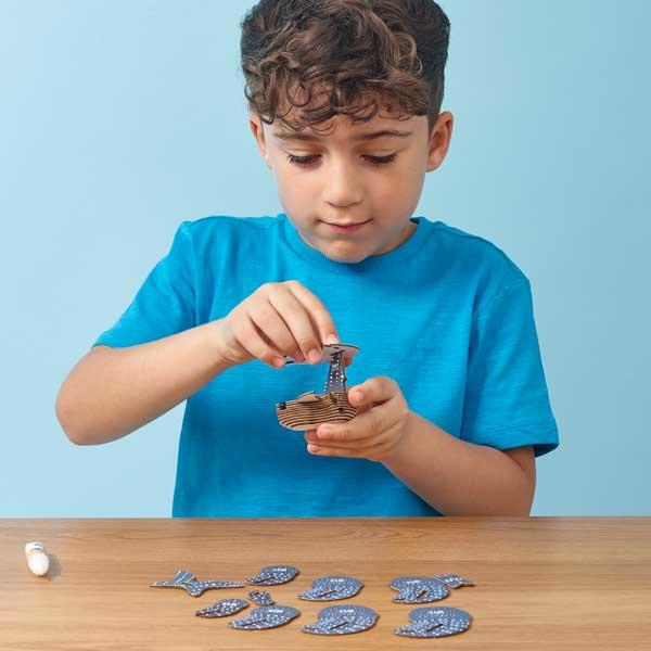 Boy in blue tshirt sitting at a table and slotting and sticking the whale shark model pieces together.