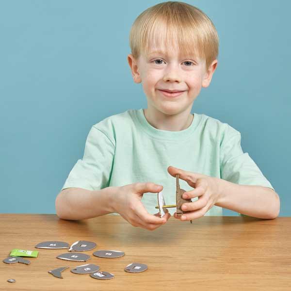 Boy with blonde hair and mint green tshirt putting pieces of dolphin craft figure together.