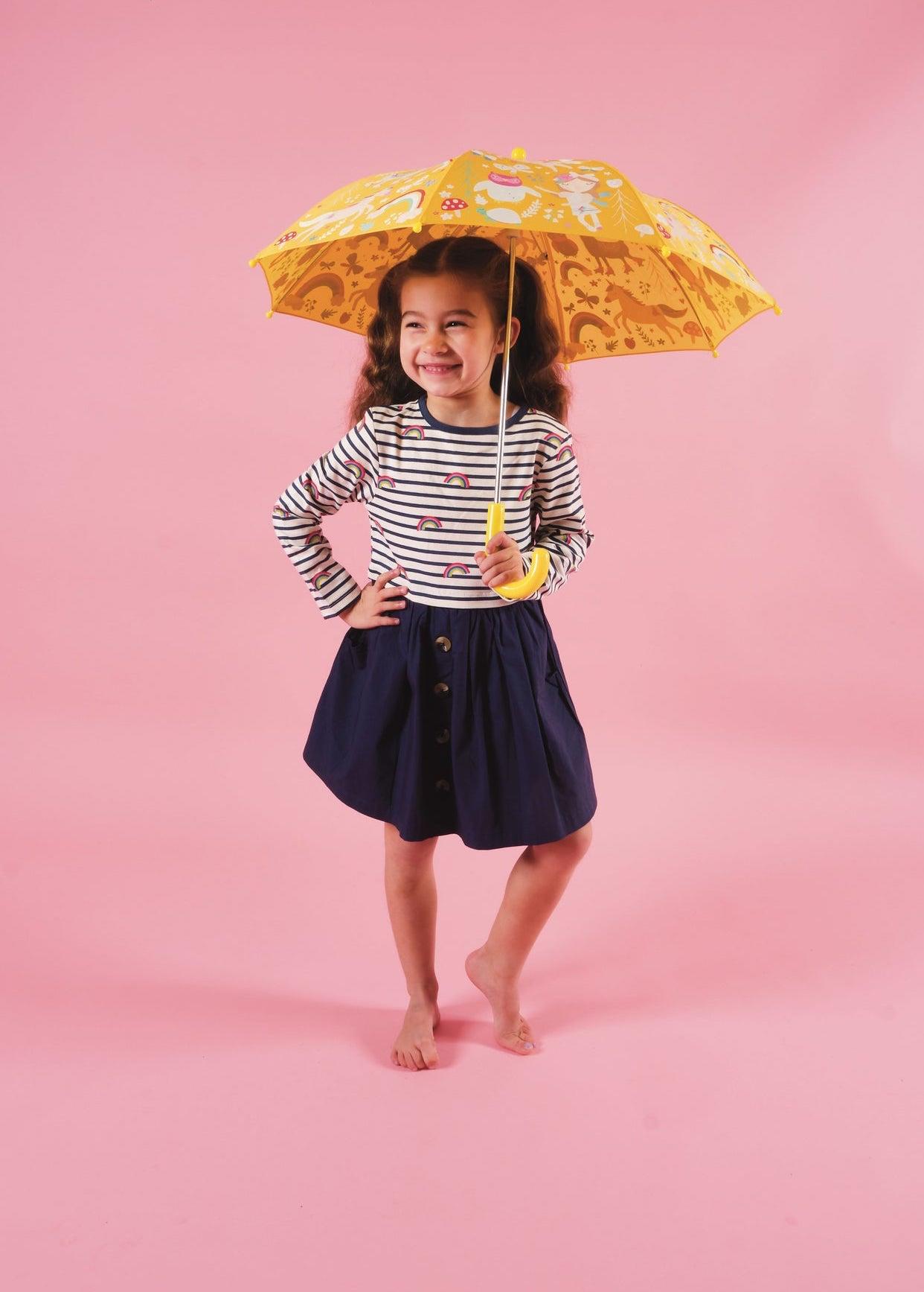Bare-footed young girl wearing a navy skirt and white and navy sttiped top holding a yellow umbrella. Pink background.
