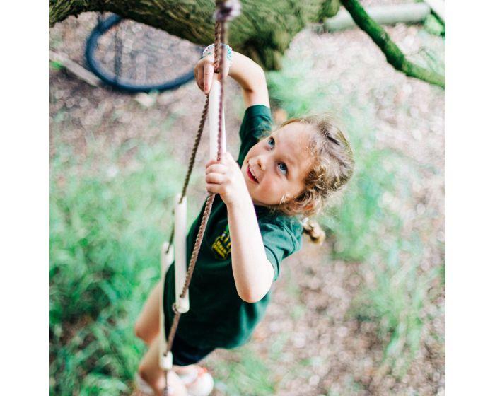 Looking down at a girl who is climbing up a rope ladder that is attached to a tree..
