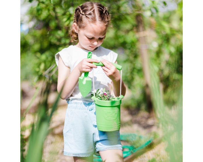 Girl wearing light blue shorts holding a green bucket and spade. Blurred garden background.