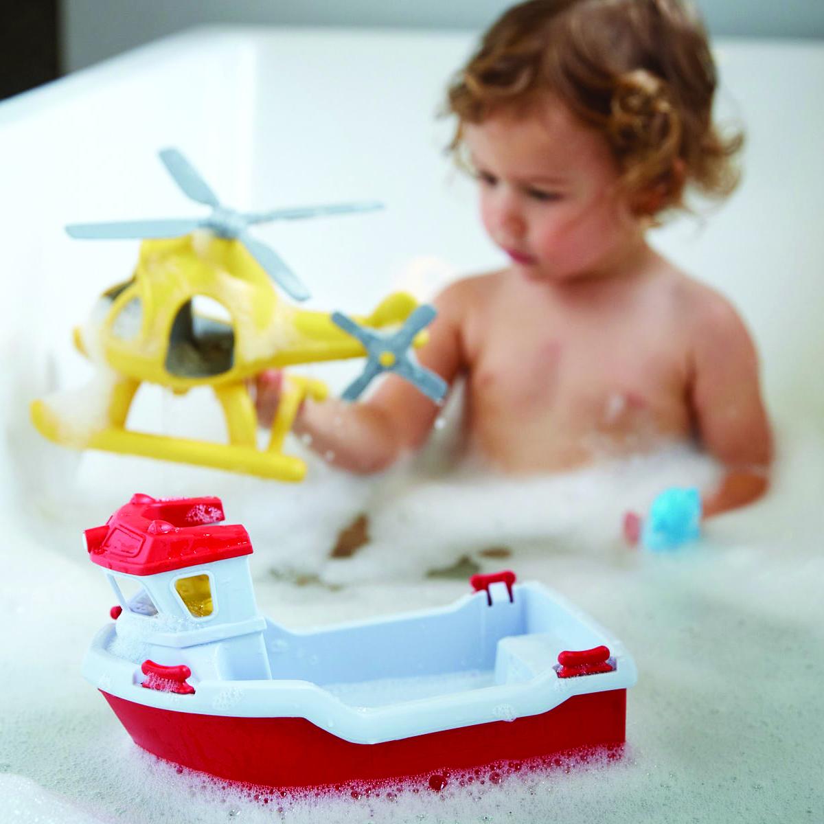 Child in a bubble bath playing with yellow helicopter and red boat.