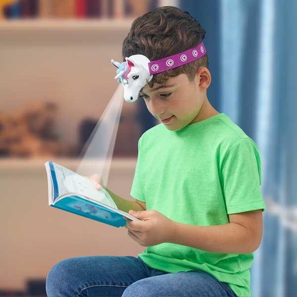 Boy in a green t-shirt reading with the unicorn head torch shining on his book.
