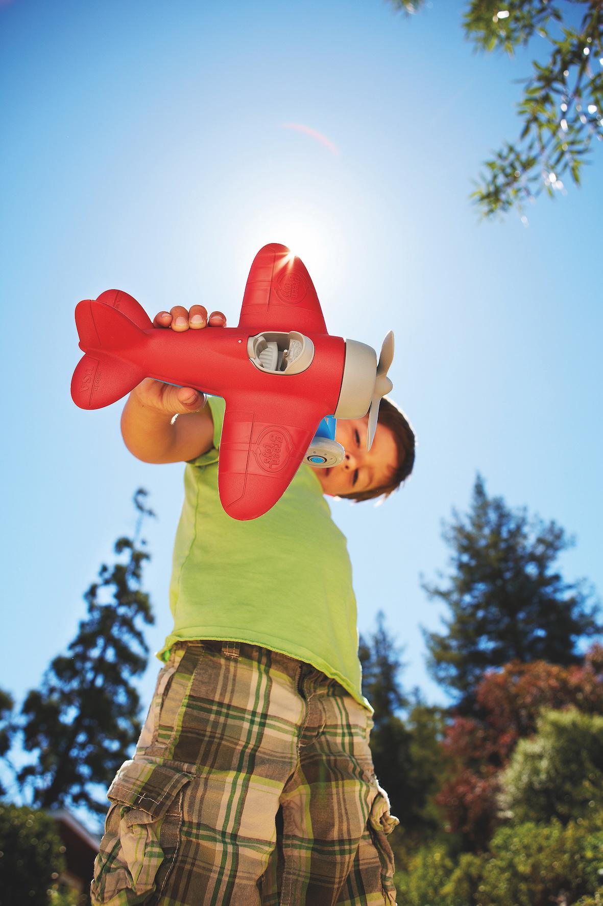 Boy playing with red airplane with blue sky in the background.