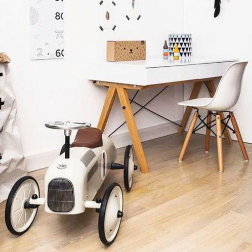 Off-white vintage car from the front in a room with wooden floors, a desk and chair.