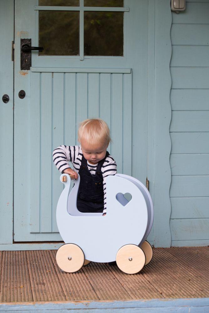 Small child in front of a light blue door with a pale blue Moover dolls' pram.