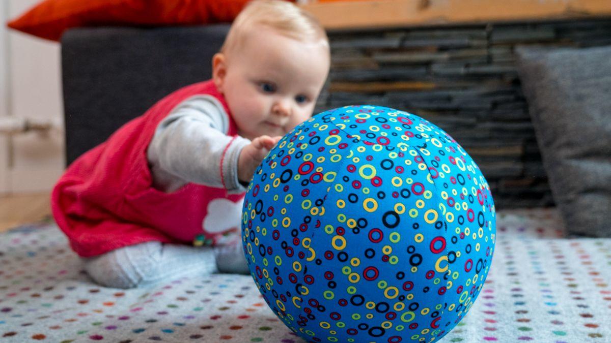 Baby reaching for a ballon encased in the blue patterned balloon cover.