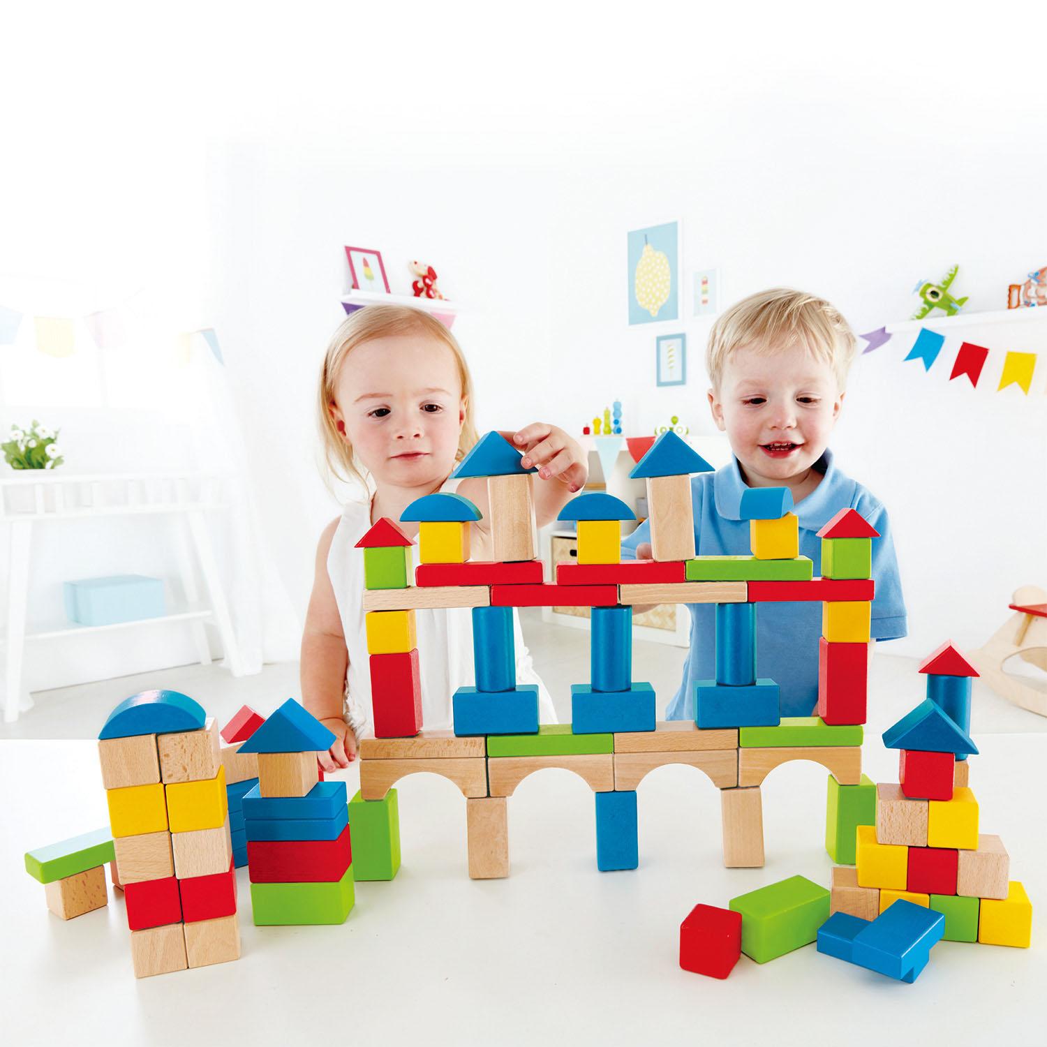 2 children placing wooden blocks on the structure in front of them. White back and foreground.