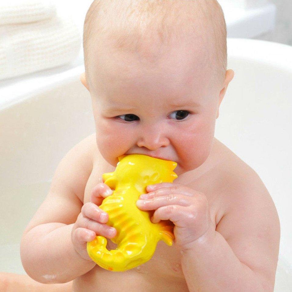 Baby in bath chewing on rubber yellow seahorse.