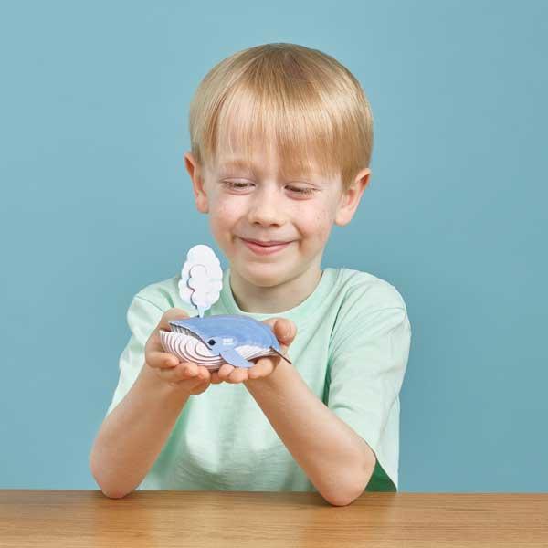 Boy with blonde hair and mint green tshirt holding out the blue whale model.
