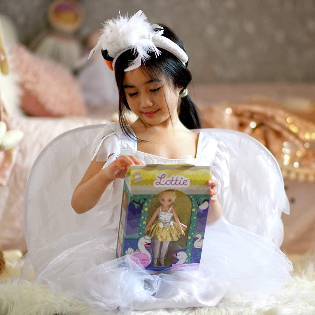 Young girl with black hair and in a white tutu opening the Lottie doll packaging.