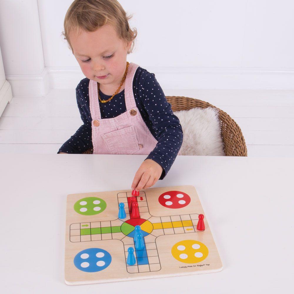 Young child in pink dungarees playing at one side of a the wooden Ludo game.