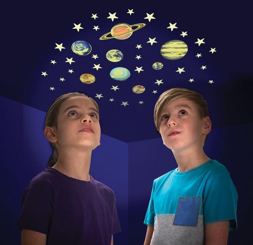 A girl and a boy with stick-on, glow in the dark.stars and planets behind them.