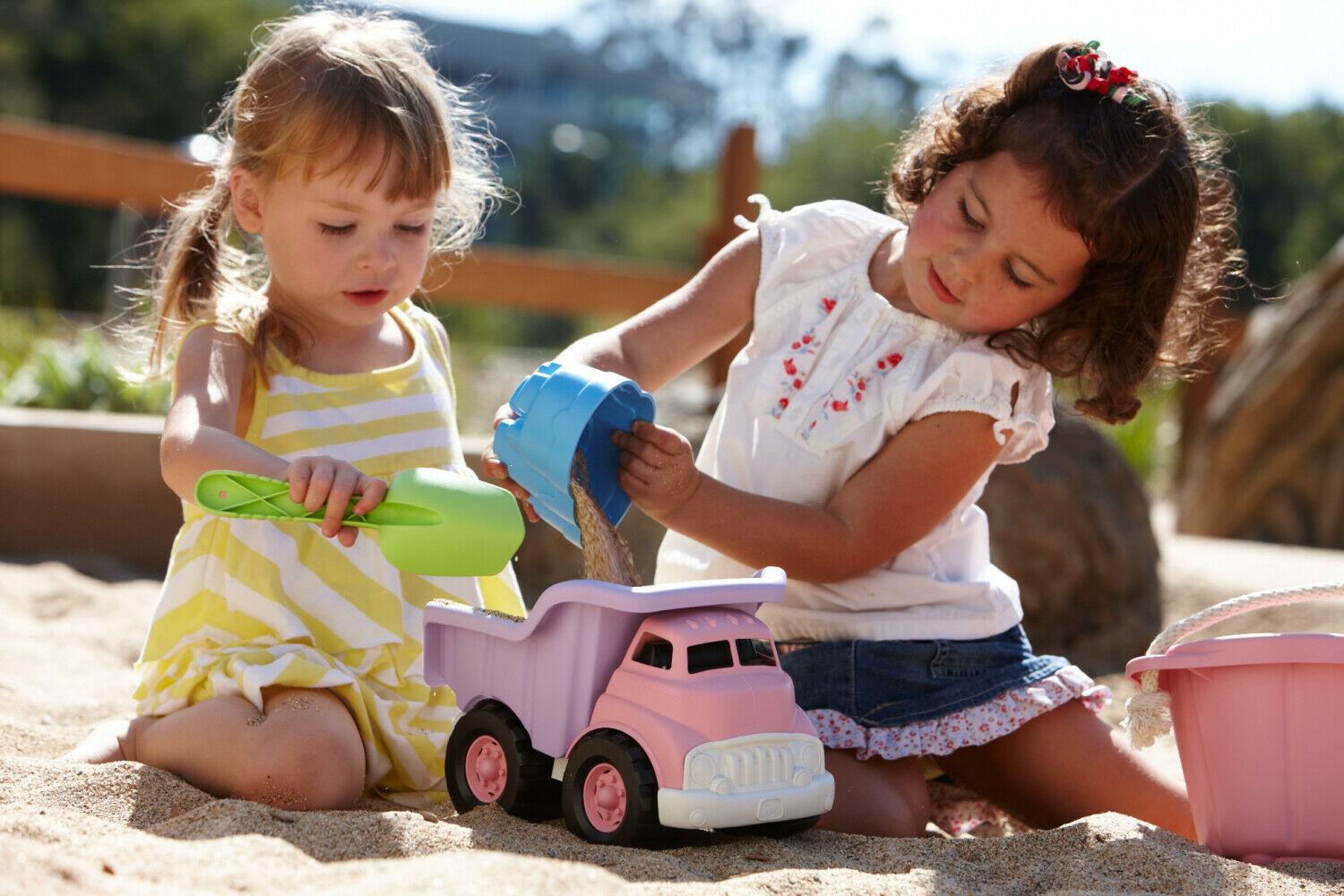 Two girls playing in a sandpit with pink dump truck.