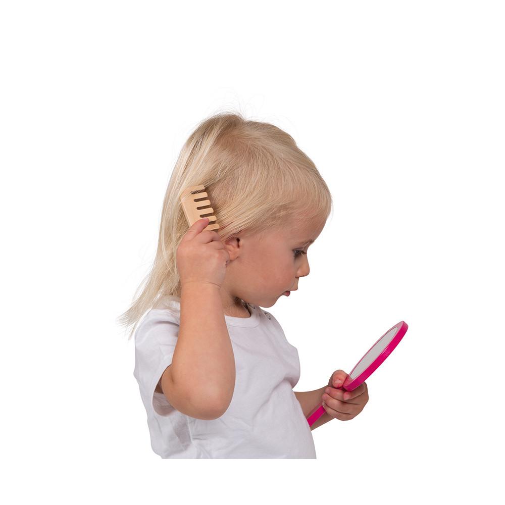 Young girl with blonde hair 'Brushing' her hair with a wooden play brush and looking into the wooden vanity mirror. White background.