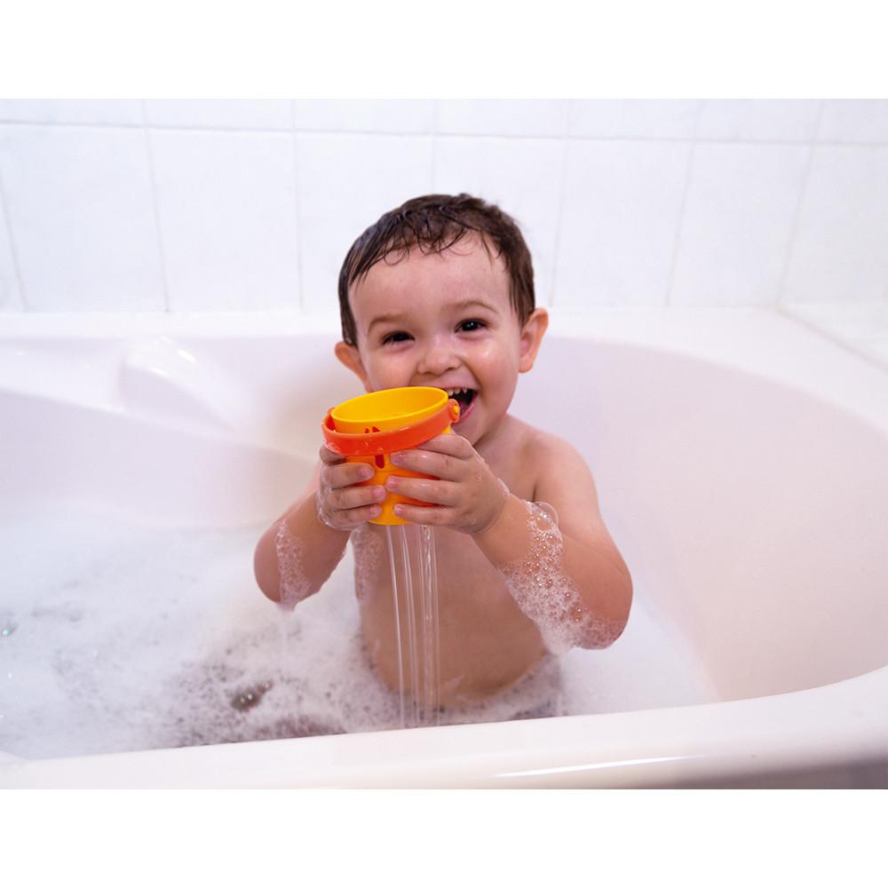 Young child in the bath laughing and playing with the orange bucket as water runs through it!