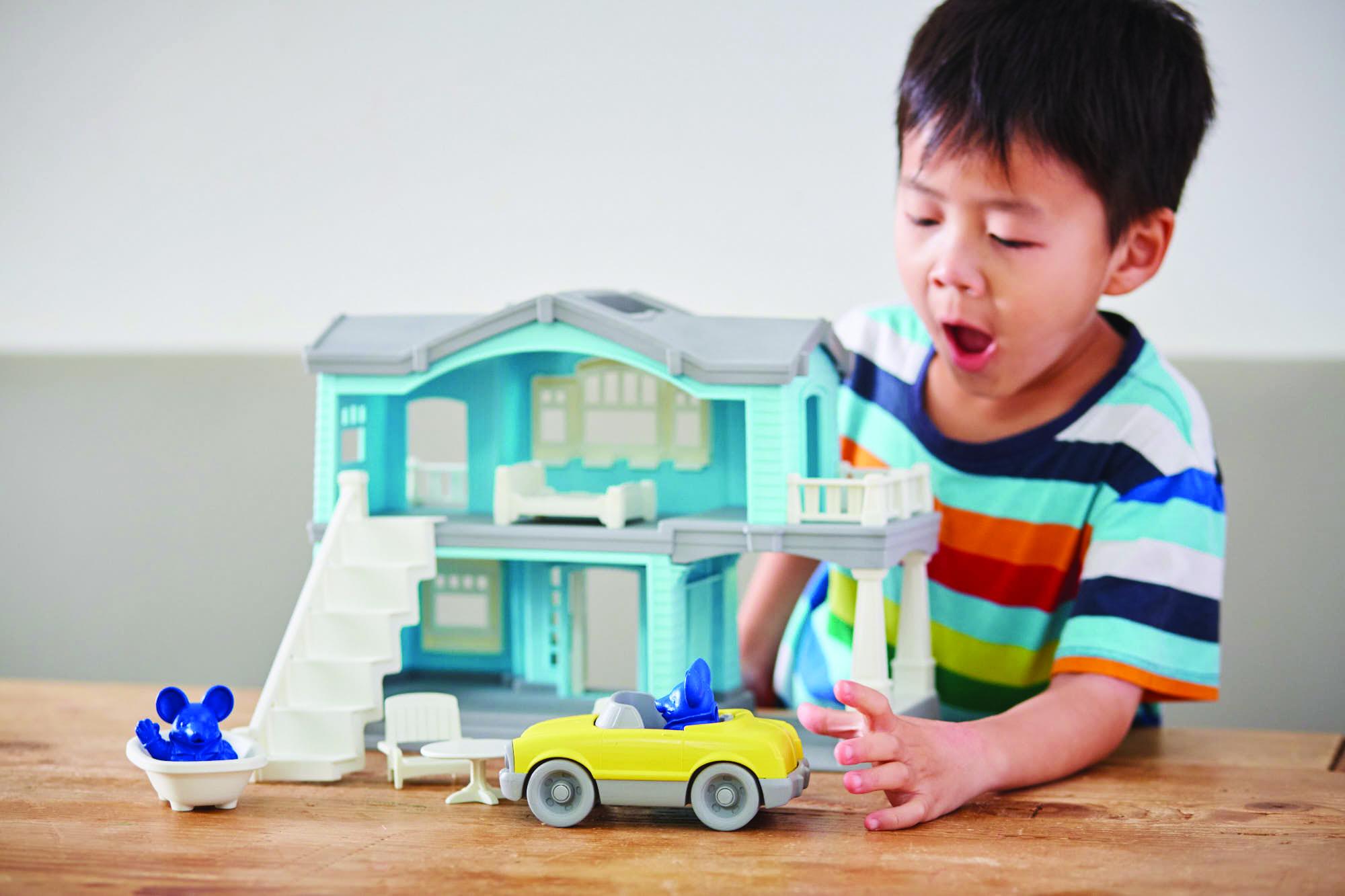 Little boy playing with blue plastic house and yellow car.
