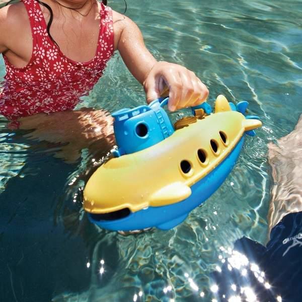 Girl in pool playing with a yellow and blue submarine that's floating on the surface.
