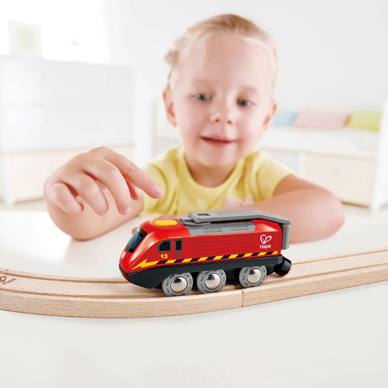 Child playing with red crank engine train on a wooden track.