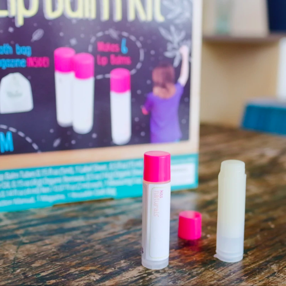 Two lip balms in tubes with packaging in background on top of wooden table.