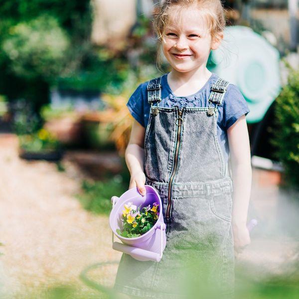 Girl in a garden holing a purple bucket.