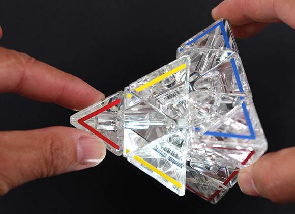 Hands moving the parts of the clear Pyraminx Crystal puzzle.