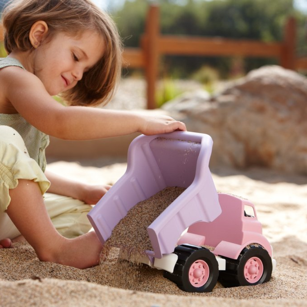 Girl playing in sandpit with pink dump truck.