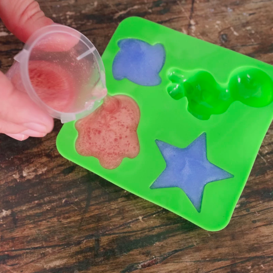 Hands pouring the soap mixture into a green silicone mould.
